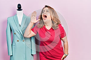 Middle age caucasian woman standing by manikin shouting and screaming loud to side with hand on mouth