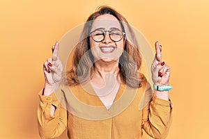 Middle age caucasian woman wearing casual clothes and glasses gesturing finger crossed smiling with hope and eyes closed