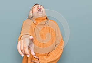 Middle age caucasian woman wearing casual winter sweater laughing at you, pointing finger to the camera with hand over body, shame