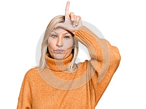 Middle age caucasian woman wearing casual winter sweater making fun of people with fingers on forehead doing loser gesture mocking