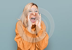 Middle age caucasian woman wearing casual winter sweater shouting angry out loud with hands over mouth