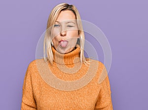 Middle age caucasian woman wearing casual winter sweater sticking tongue out happy with funny expression