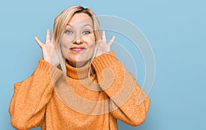 Middle age caucasian woman wearing casual winter sweater trying to hear both hands on ear gesture, curious for gossip