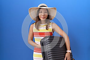 Middle age chinese woman holding suitcase going on summer vacation looking positive and happy standing and smiling with a