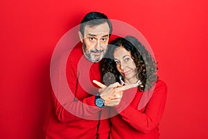 Middle age couple of hispanic woman and man hugging and standing together pointing to both sides with fingers, different direction