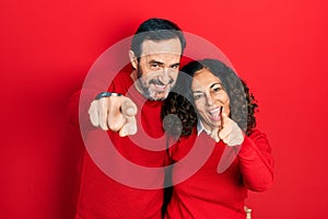 Middle age couple of hispanic woman and man hugging and standing together pointing to you and the camera with fingers, smiling