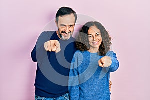 Middle age couple of hispanic woman and man hugging and standing together pointing to you and the camera with fingers, smiling