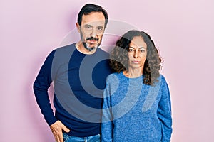 Middle age couple of hispanic woman and man hugging and standing together relaxed with serious expression on face