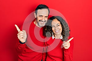 Middle age couple of hispanic woman and man hugging and standing together smiling confident pointing with fingers to different