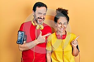 Middle age couple of hispanic woman and man wearing sportswear and arm band cheerful with a smile of face pointing with hand and