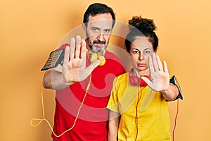 Middle age couple of hispanic woman and man wearing sportswear and arm band doing stop sing with palm of the hand