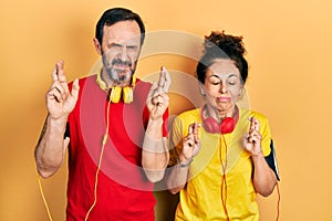 Middle age couple of hispanic woman and man wearing sportswear and arm band gesturing finger crossed smiling with hope and eyes