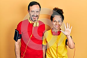 Middle age couple of hispanic woman and man wearing sportswear and arm band showing and pointing up with fingers number five while
