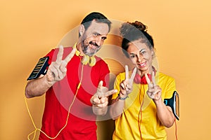 Middle age couple of hispanic woman and man wearing sportswear and arm band smiling looking to the camera showing fingers doing