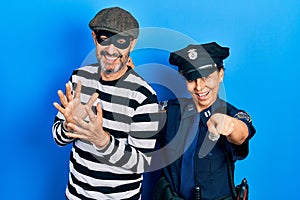 Middle age couple of hispanic woman and man wearing thief and police uniform pointing to you and the camera with fingers, smiling