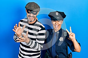 Middle age couple of hispanic woman and man wearing thief and police uniform smiling looking to the camera showing fingers doing