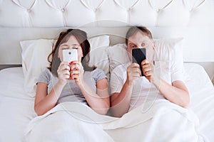 Middle age couple hold cell phones in bedroom, modern family photo