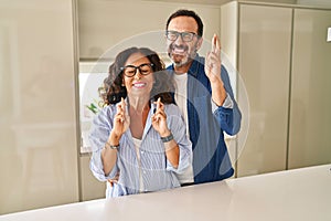 Middle age couple standing together gesturing finger crossed smiling with hope and eyes closed