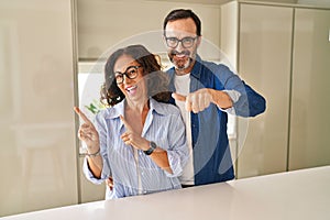 Middle age couple standing together pointing to the back behind with hand and thumbs up, smiling confident