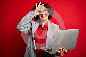 Middle age curly hair business woman working using laptop over  red background with happy face smiling doing ok sign with