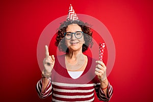 Middle age curly hair woman wearing birthday funny hat holding party trumpet on celebration surprised with an idea or question