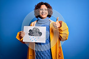 Middle age curly hair woman wearing rain coat holding banner with cloud over blue background happy with big smile doing ok sign,