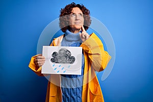 Middle age curly hair woman wearing rain coat holding banner with cloud over blue background serious face thinking about question,