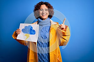 Middle age curly hair woman wearing rain coat holding banner with cloud and thunder surprised with an idea or question pointing