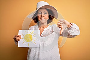 Middle age curly woman on vacation holding bunner with sun image over yellow background with angry face, negative sign showing