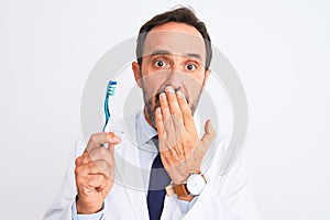 Middle age dentist man holding toothbrush standing over isolated white background cover mouth with hand shocked with shame for