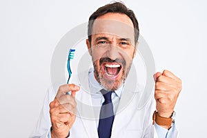 Middle age dentist man holding toothbrush standing over isolated white background screaming proud and celebrating victory and