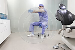 Middle age,dentist  stretching arms sitting on dental saddle