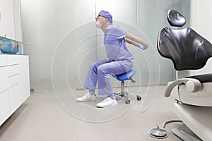 Middle age,dentist  stretching arms sitting on dental saddle