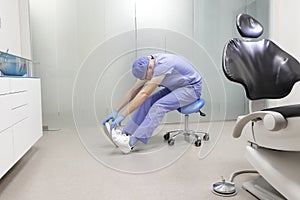 Middle age,dentist  stretching legs, arms,back sitting on dental saddle - back view