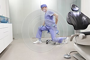 Middle age,dentist  stretching legs sitting on dental saddle