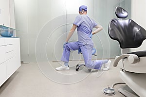 Middle age,dentist  stretching legs sitting on dental saddle - back view
