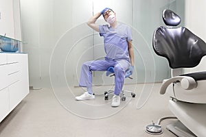 Middle age,dentist  stretching neck sitting on dental saddle