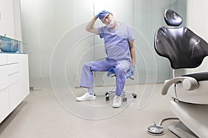 Middle age,dentist  stretching neck sitting on dental saddle