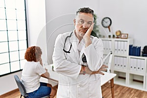 Middle age doctor man at the clinic with a patient thinking looking tired and bored with depression problems with crossed arms