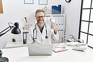 Middle age doctor man holding thermometer at the clinic looking positive and happy standing and smiling with a confident smile