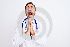 Middle age doctor man wearing coat and stethoscope standing over isolated white background begging and praying with hands together
