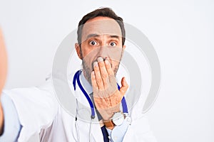 Middle age doctor man wearing stethoscope make selfie over isolated white background cover mouth with hand shocked with shame for