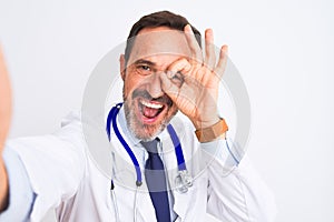 Middle age doctor man wearing stethoscope make selfie over isolated white background with happy face smiling doing ok sign with