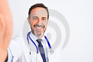Middle age doctor man wearing stethoscope make selfie over isolated white background with a happy face standing and smiling with a