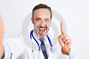 Middle age doctor man wearing stethoscope make selfie over isolated white background surprised with an idea or question pointing