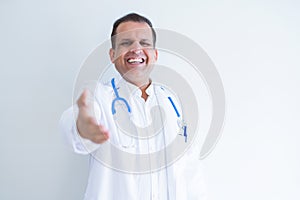 Middle age doctor man wearing stethoscope and medical coat over white background smiling friendly offering handshake as greeting