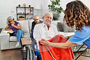 Middle age doctor woman supporting retired man sitting on wheelchair at nursing home