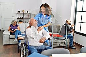 Middle age doctor woman supporting retired man sitting on wheelchair at nursing home