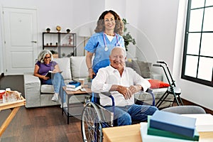 Middle age doctor woman supporting retired man sitting on wheelchair at nursing home