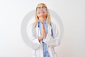 Middle age doctor woman wearing glasses and stethoscope over isolated white background begging and praying with hands together